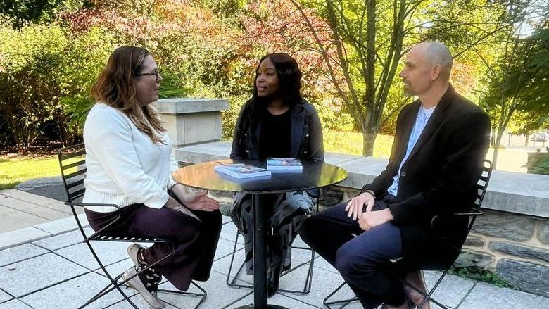 Three people around an outdoor table talking